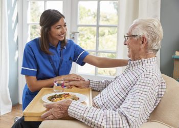Nurse serving dinner to a senior man in an armchair at home