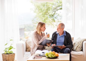 Health visitor and a senior man with tablet during home visit.