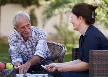 Professional helpful caregiver and a senior man during home visit
